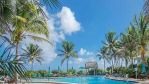 Un área de piscina con sillones de descanso y palmeras.