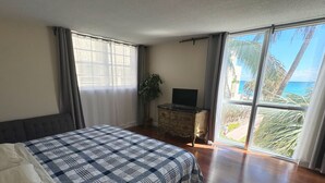 Un dormitorio con una cama grande, un televisor sobre un aparador de madera y vista al océano a través de amplias ventanas.