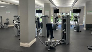 Un gimnasio con diversas máquinas de ejercicio, ventanas amplias y techo de baldosas.