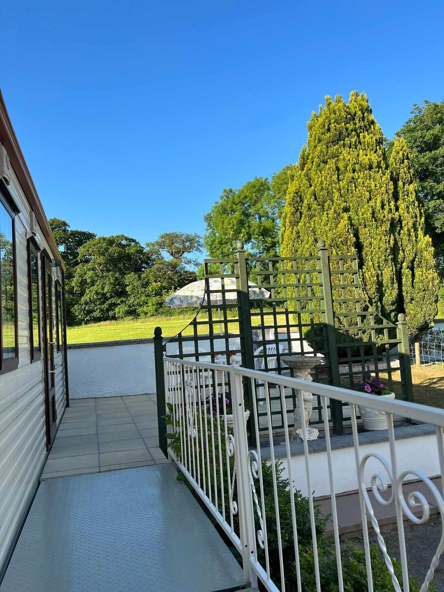 A covered outdoor area with a metal railing, a stone bench, and a view of a green landscape.