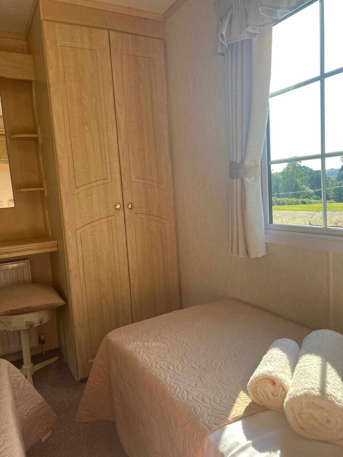 Een slaapkamer met een grote houten garderobe, een bed met een bloemenbedekking en een raam met uitzicht op groen.