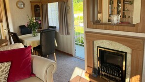 A cozy living area with a fireplace, a dining table with chairs, and a sofa with a red cushion. - Heavenly Retreat - spacious & peaceful with patio (Ciliau Aeron)