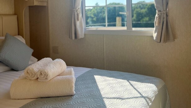 A neatly made bed with rolled towels, a window with curtains, and a view of greenery outside. - Heavenly Retreat - spacious & peaceful with patio (Ciliau Aeron)