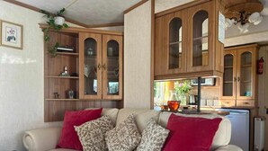 A living room with a beige sofa, patterned cushions, and a red throw. There are wooden cabinets with glass doors, a small table, and a ceiling fan. - Heavenly Retreat - spacious & peaceful with patio (Ciliau Aeron)
