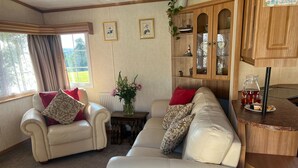 A cozy living room with two white leather sofas, a wooden cabinet, and a small table with a vase of flowers. - Heavenly Retreat - spacious & peaceful with patio (Ciliau Aeron)
