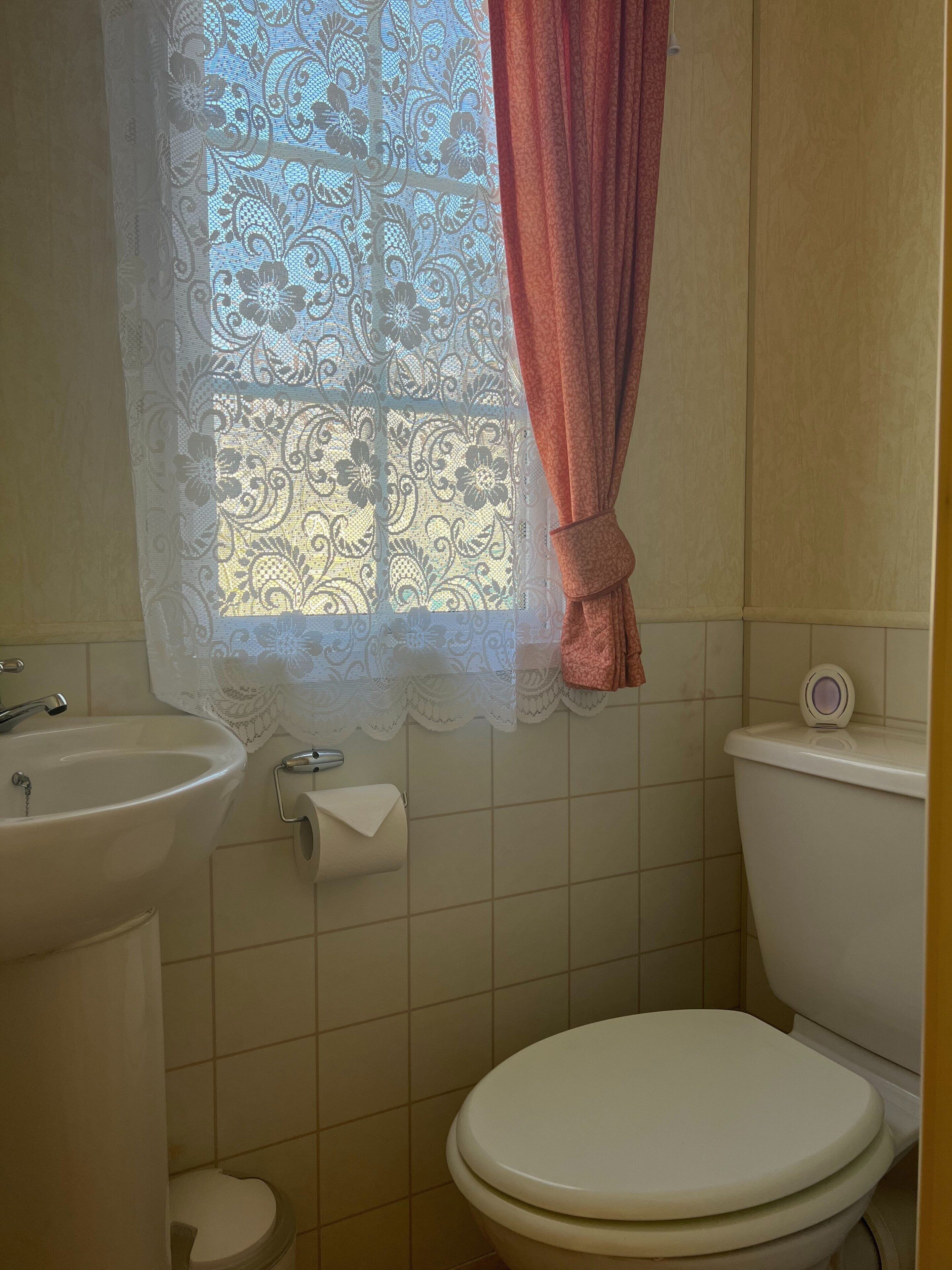 A bathroom with a sink, toilet, and window with lace curtains.