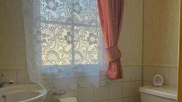 A bathroom with a sink, toilet, and window with lace curtains.