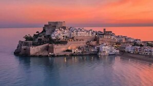 A coastal town with a fortified castle, white buildings, and a calm sea at sunset. - Peniscola Intramuros Suites (Peñíscola)
