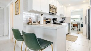 Une cuisine moderne avec des meubles blancs, un îlot central et des tabourets de bar verts.