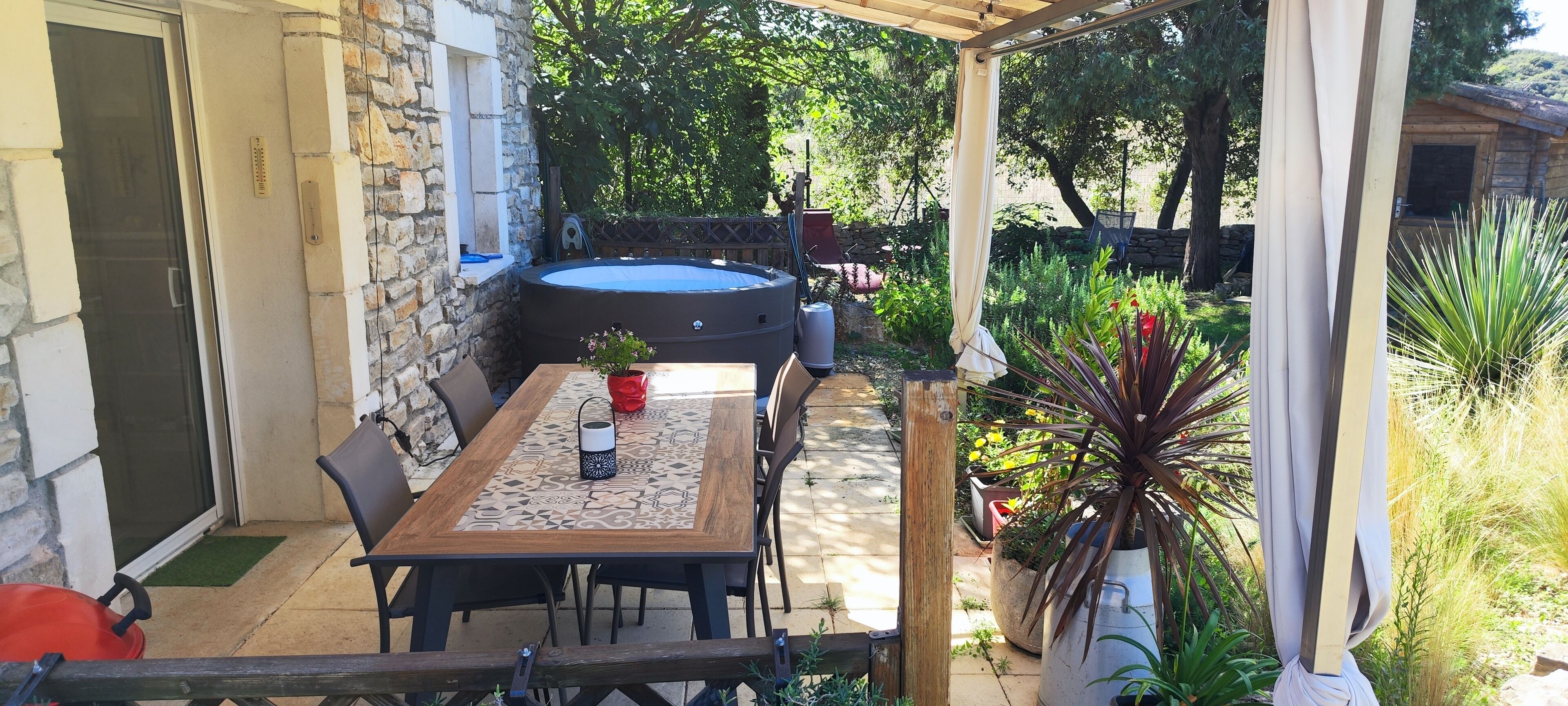 Un patio con mesa y sillas, un jacuzzi y un jardín con diversas plantas.