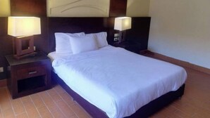 Una cama bien hecha con sábanas blancas, dos mesitas de noche con lámparas y un cabecero oscuro.