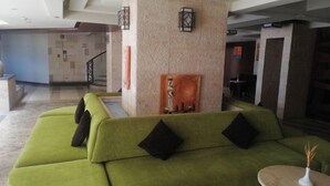 Un sofá verde con cojines negros en un área de recepción con suelo de baldosas y una obra de arte colgada en la pared.