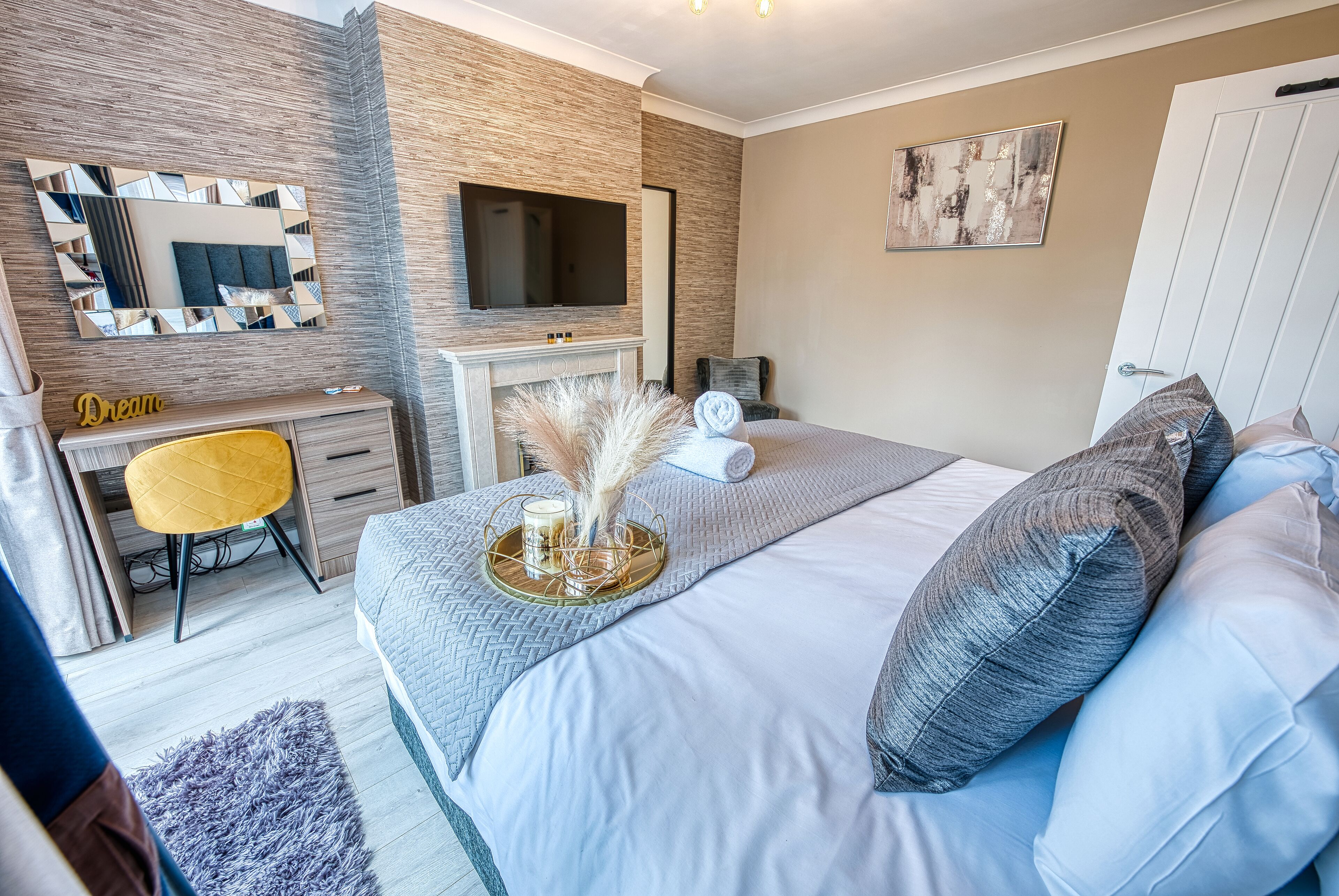 A bedroom with a bed, a desk, a chair, a TV, and a door.