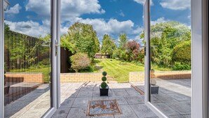 A view from a glass door into a garden with a lawn, trees, and a brick wall. - Maple House (Solihull)