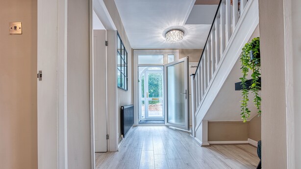 A spacious hallway with a wooden floor, a chandelier, and a view to the outdoors. - Maple House (Solihull)