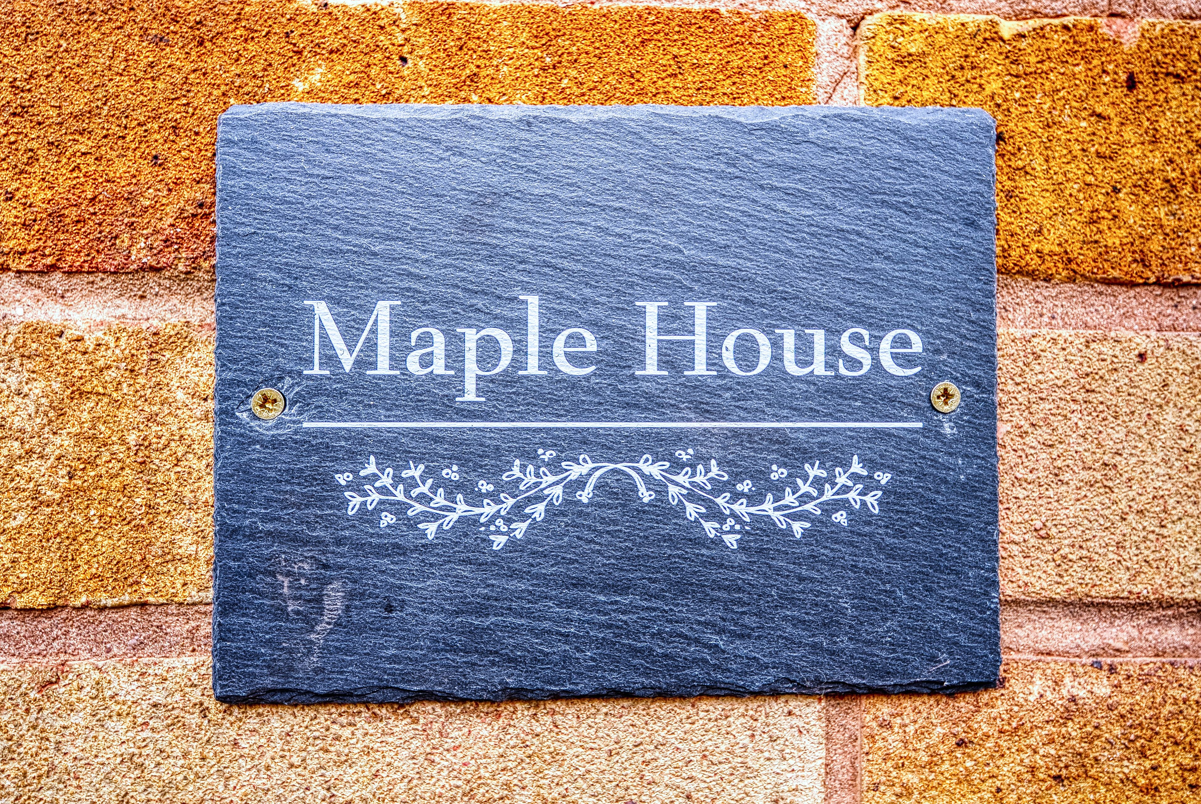 A slate sign with "Maple House" written on it, mounted on a brick wall.