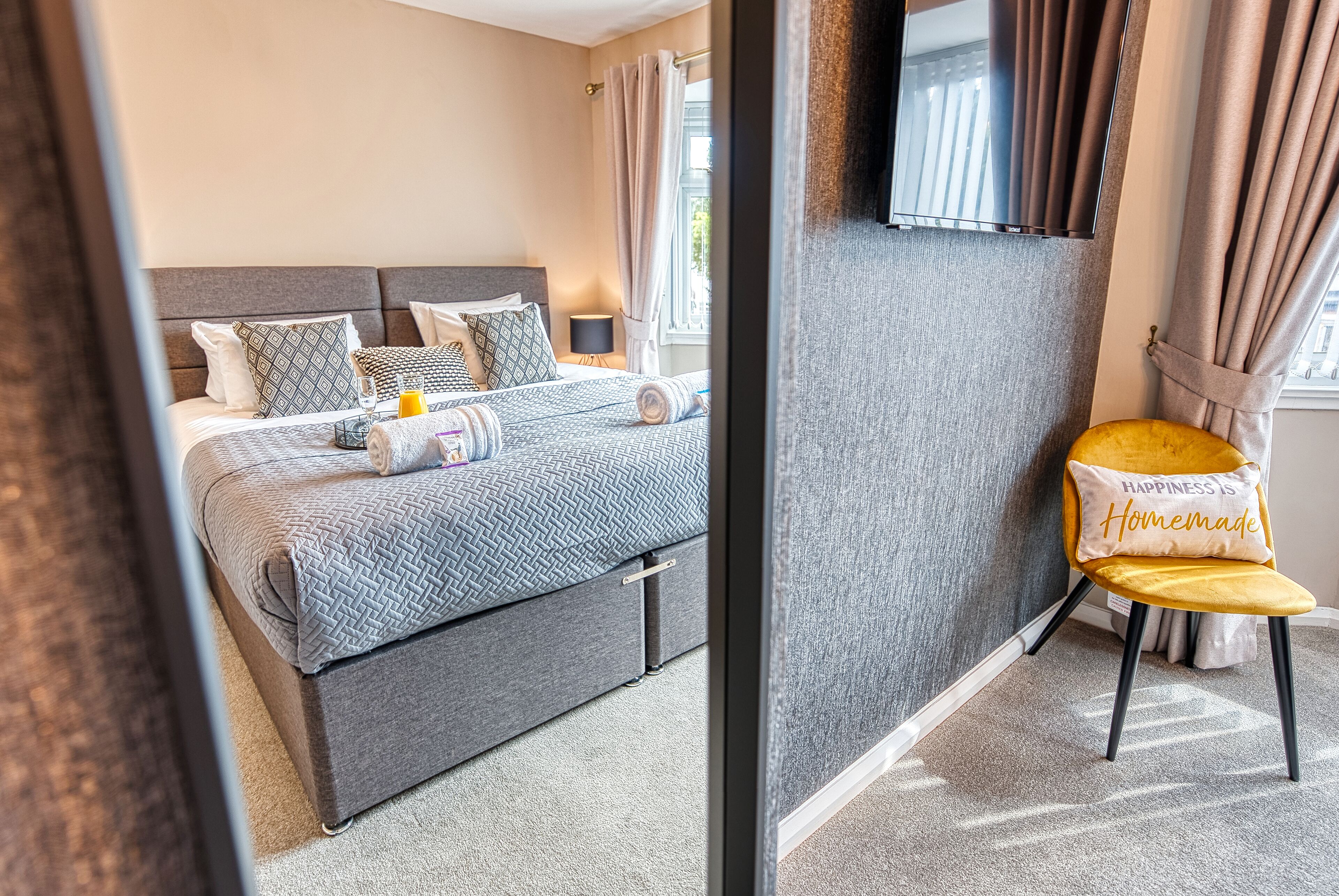 Un dormitorio ordenado con cama, mesita de noche y una silla con cojín.