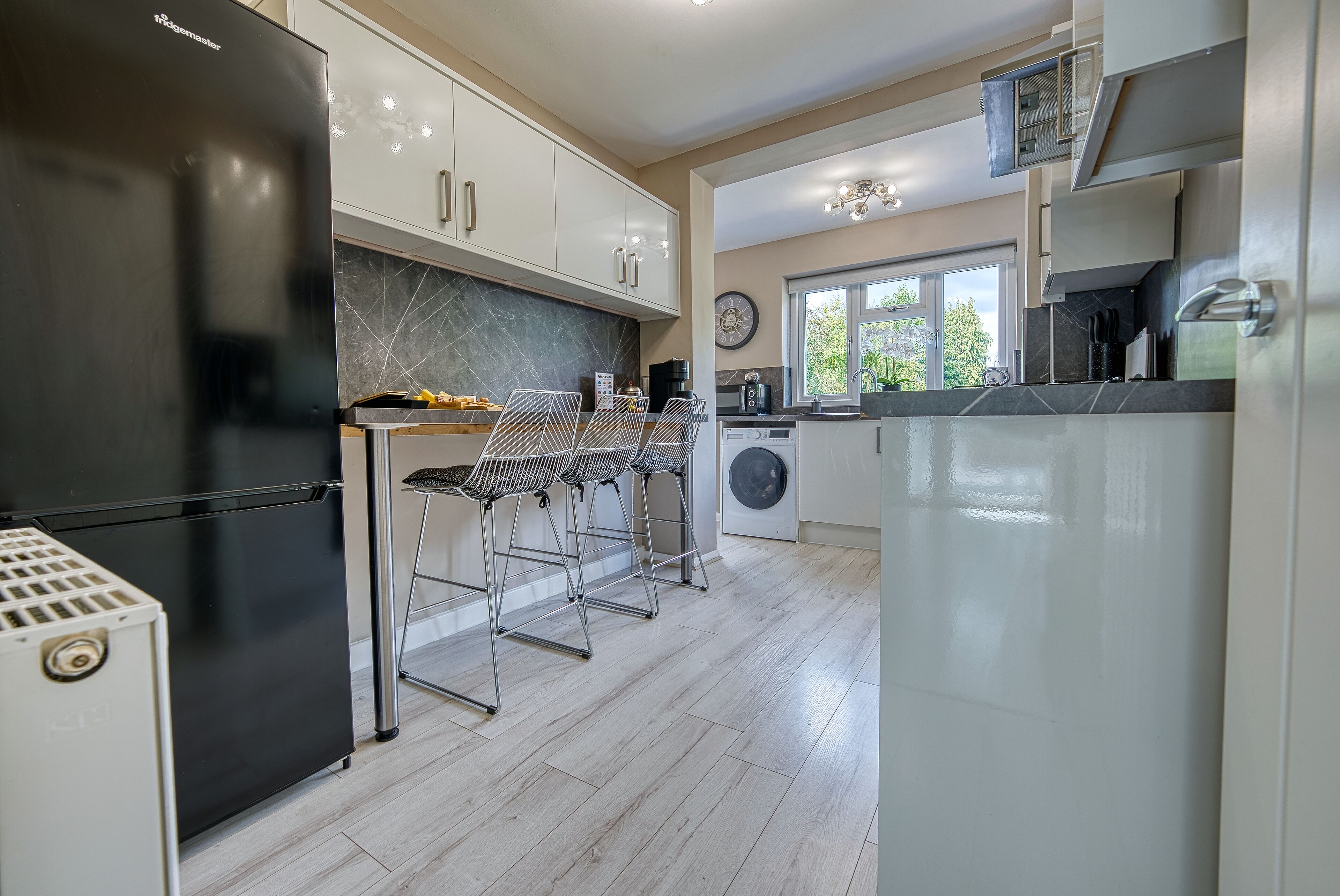 A modern kitchen with a black refrigerator, white cabinets, and a dining area with metal chairs.