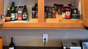 A kitchen cabinet with shelves holding glassware, plates, and various condiments. - FALL & WINTER BONUS — POOL HEAT INCLUDED NOVEMBER 1-MARCH 31 (Indio)