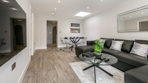 Una sala moderna con una mesa de centro de vidrio, un sofá de cuero negro y una zona de comedor con una mesa y sillas de vidrio.