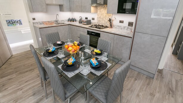 Una cocina moderna con armarios grises, una mesa de comedor de cristal con sillas y una isla central con frutero.