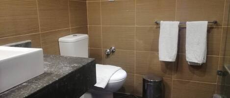 Une salle de bain comprenant des toilettes, un lavabo, une poubelle et deux serviettes suspendues à un porte-serviettes.