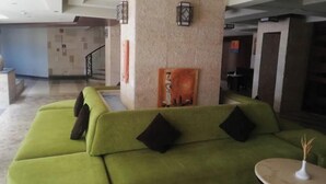 Un sofá verde con cojines negros en un área de recepción con suelo de baldosas y una mesa de mármol con un florero.
