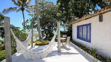 A hammock tied between wooden posts, a table and chairs, and a building with blue-framed windows.