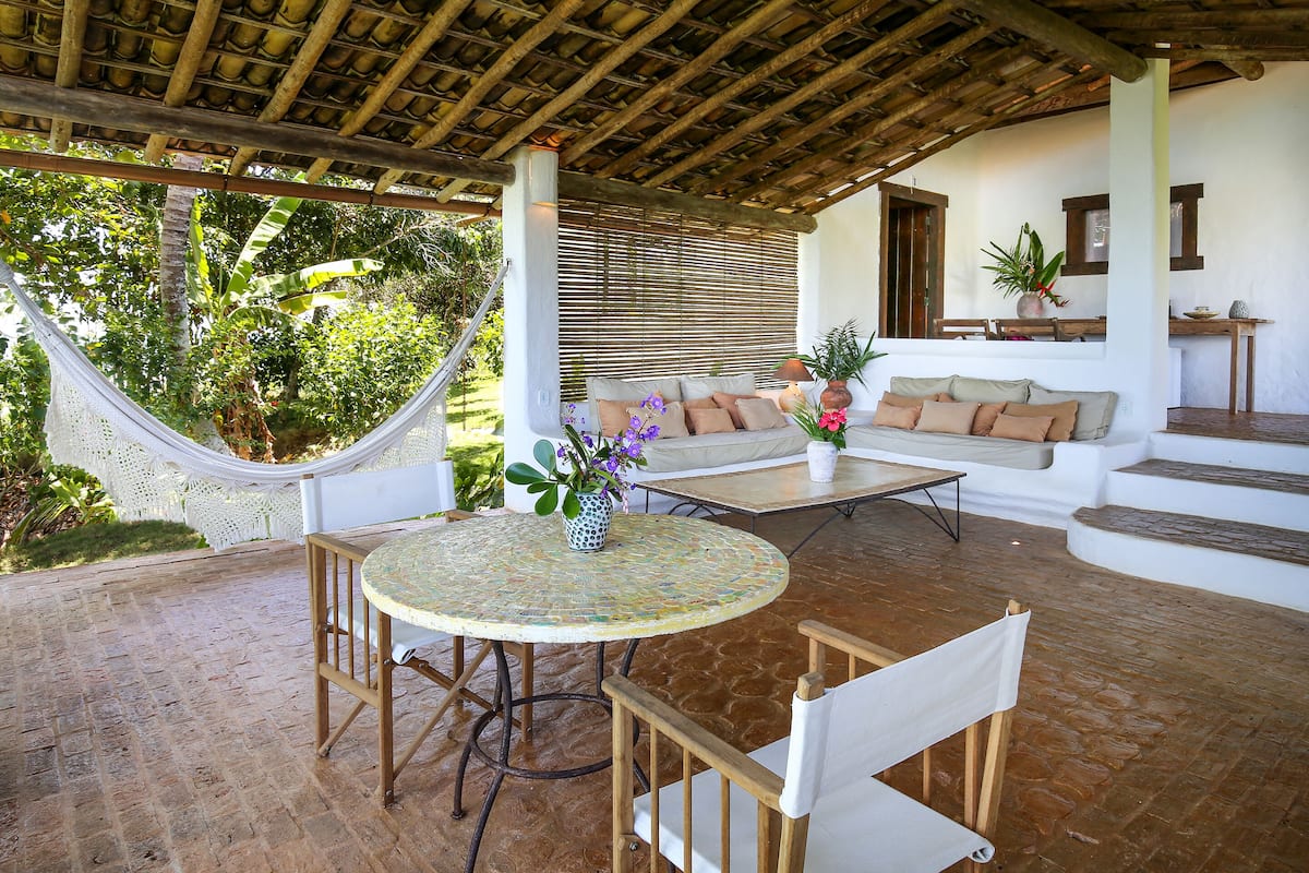 A covered patio with a round table, two sofas, and a hammock.
