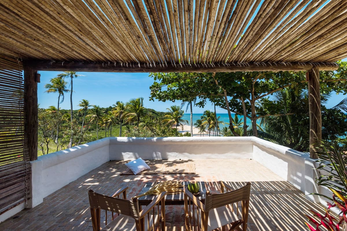 A covered outdoor seating area with a view of the beach and palm trees.
