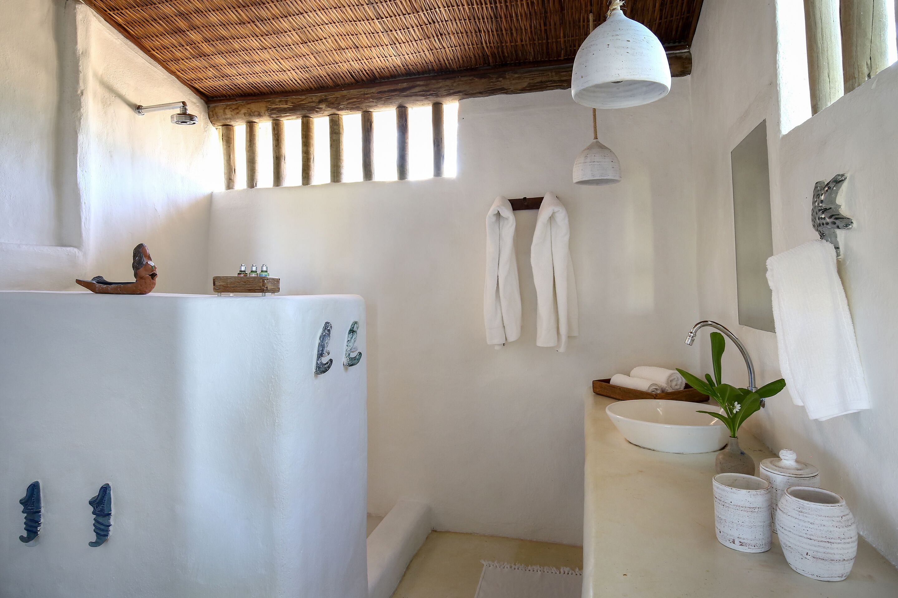 Une salle de bain avec une baignoire, un lavabo et une douche. Des serviettes sont accrochées au mur et une plante est posée sur le lavabo.