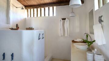 Une salle de bain avec une baignoire, un lavabo et une douche. Des serviettes sont accrochées au mur et une plante est posée sur le lavabo.