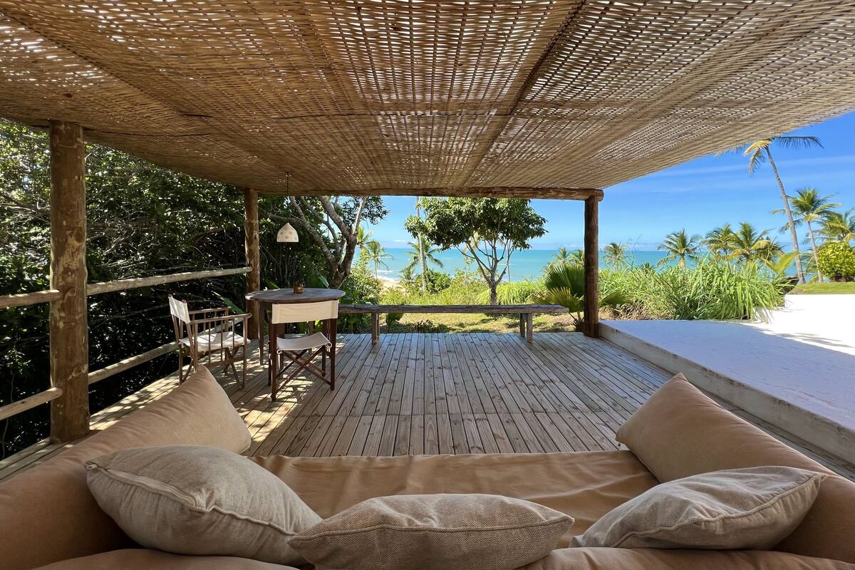A wooden deck with a woven canopy, a cushioned seating area, and a table with chairs.
