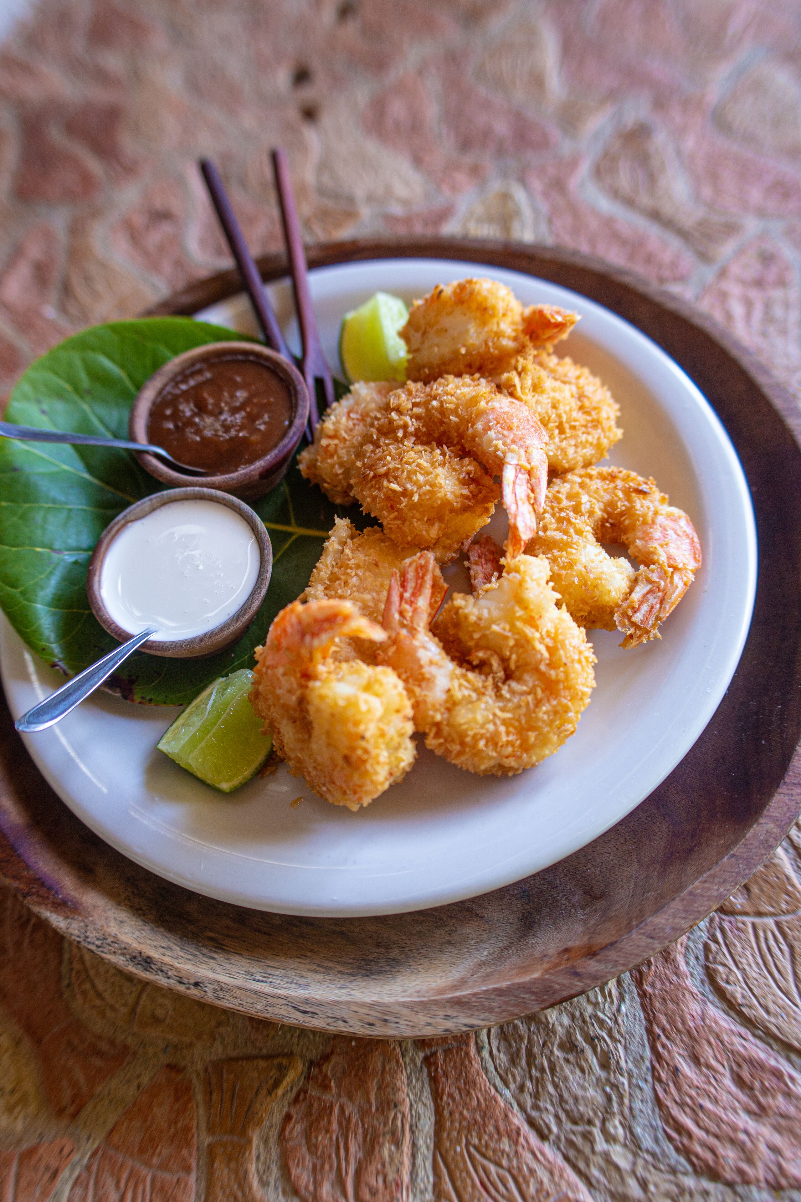 A plate of fried shrimp with dipping sauces and lime wedges.