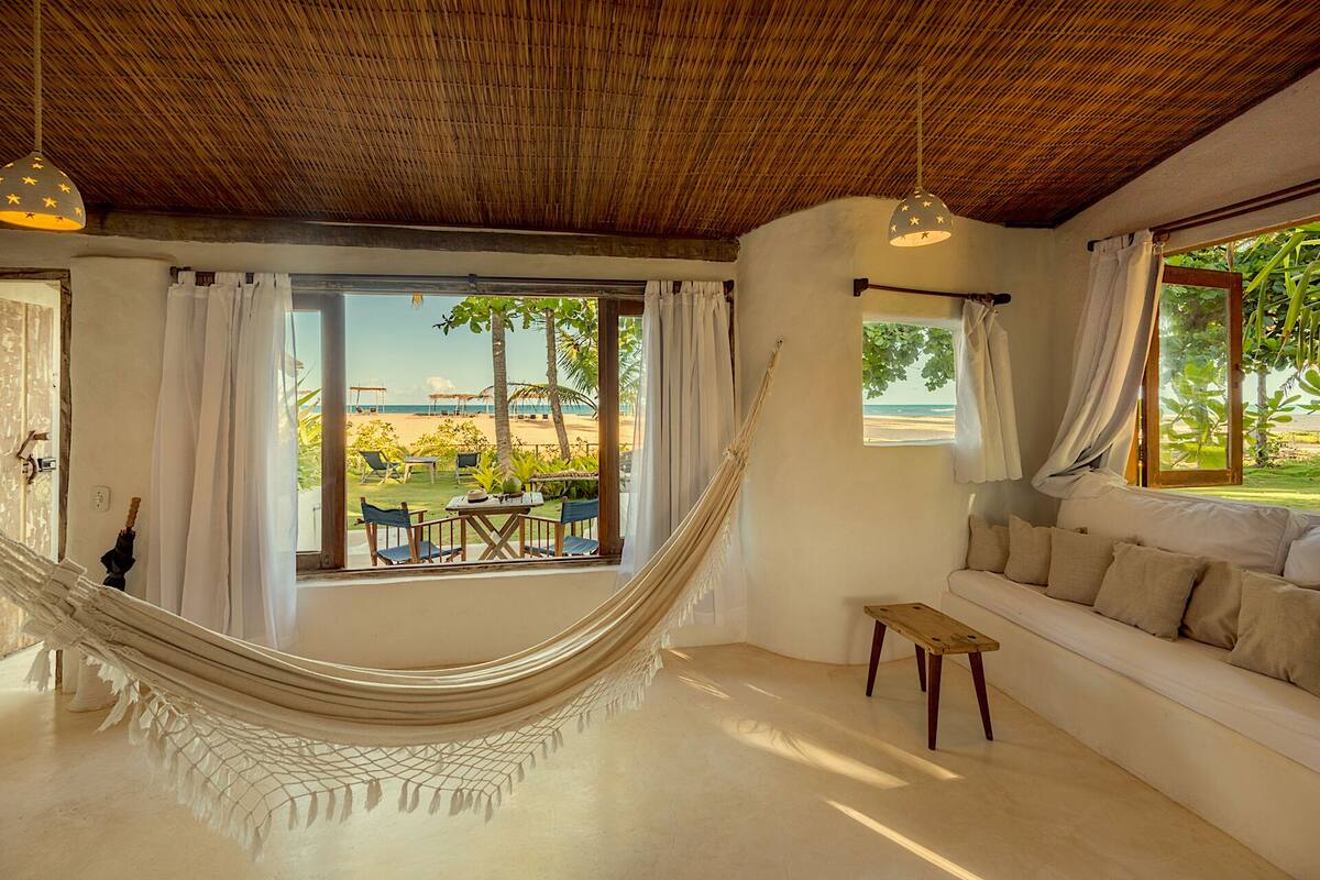 A room with a hammock, a sofa, and a view of the beach.