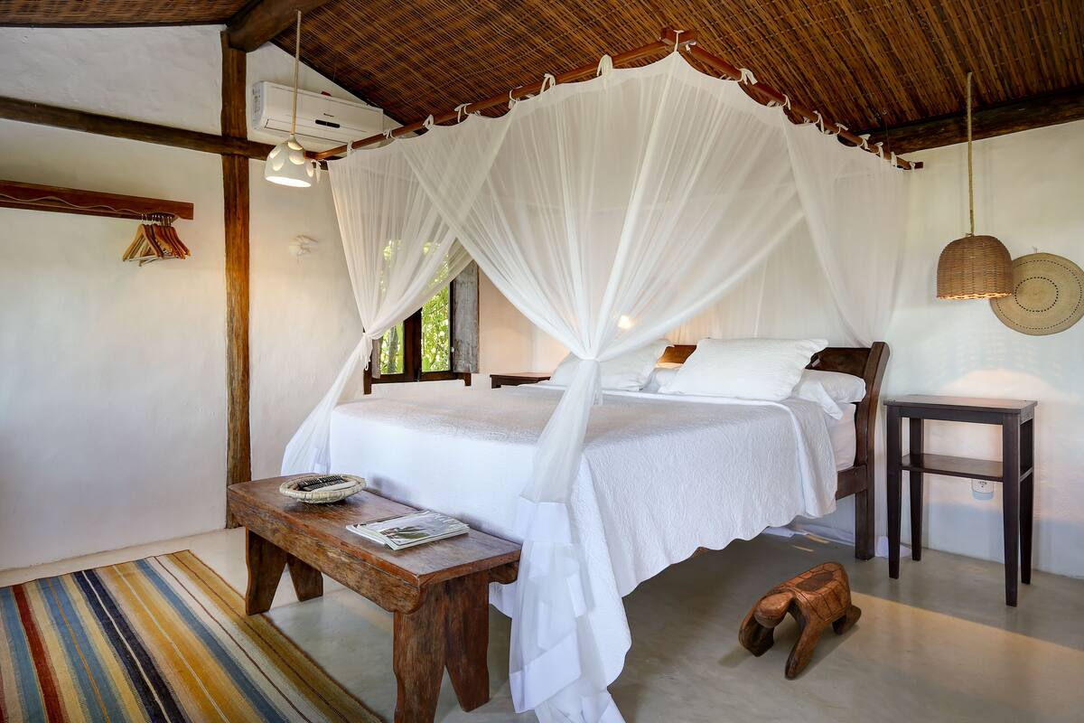 A bedroom with a canopy bed, a wooden bench, a small table, and a wall-mounted shelf.