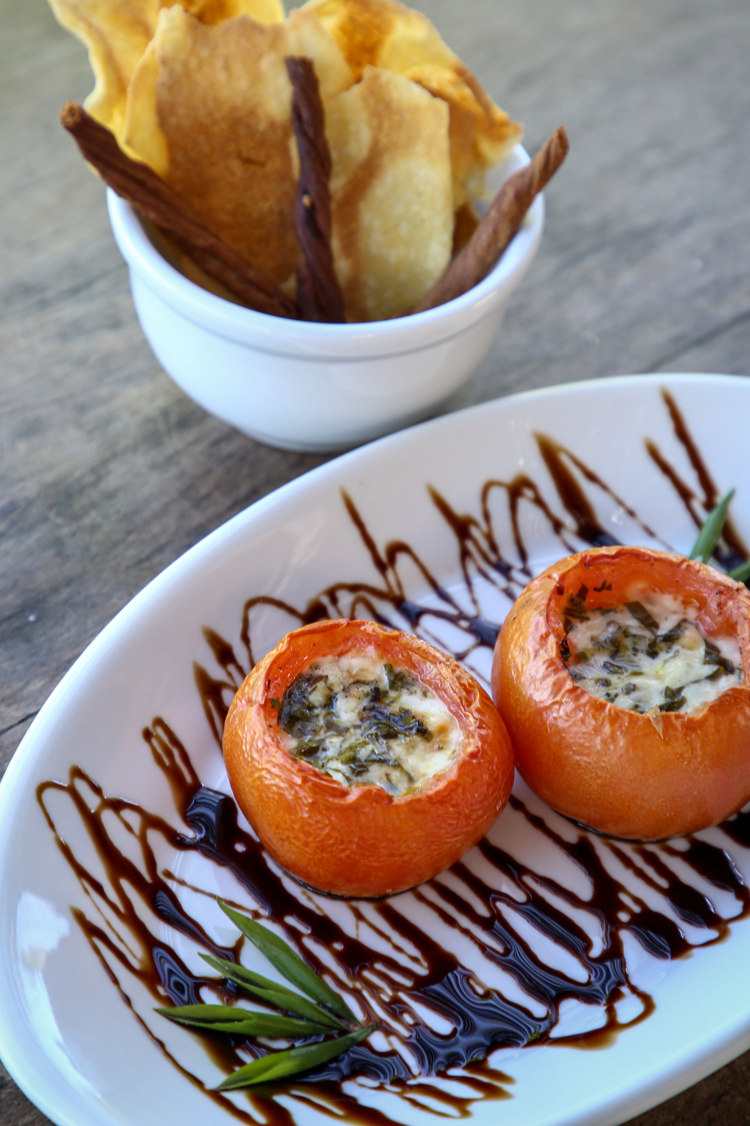 Um prato com tomate recheado e, ao fundo, uma tigela de batatas fritas.