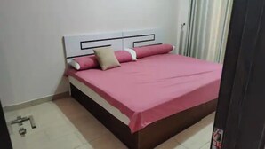 A bed with a white headboard and pink bedding, a door to the right, and a tiled floor.