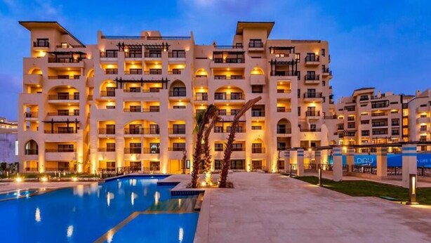 A multi-story hotel with a swimming pool and well-lit balconies. - Luxury Apartment in ALDAU HEIGHTS 10204 (Hurghada)