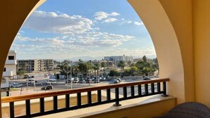 A balcony with a view of a busy street, buildings, and a clear sky. - Luxury Apartment in ALDAU HEIGHTS 10204 (Hurghada)