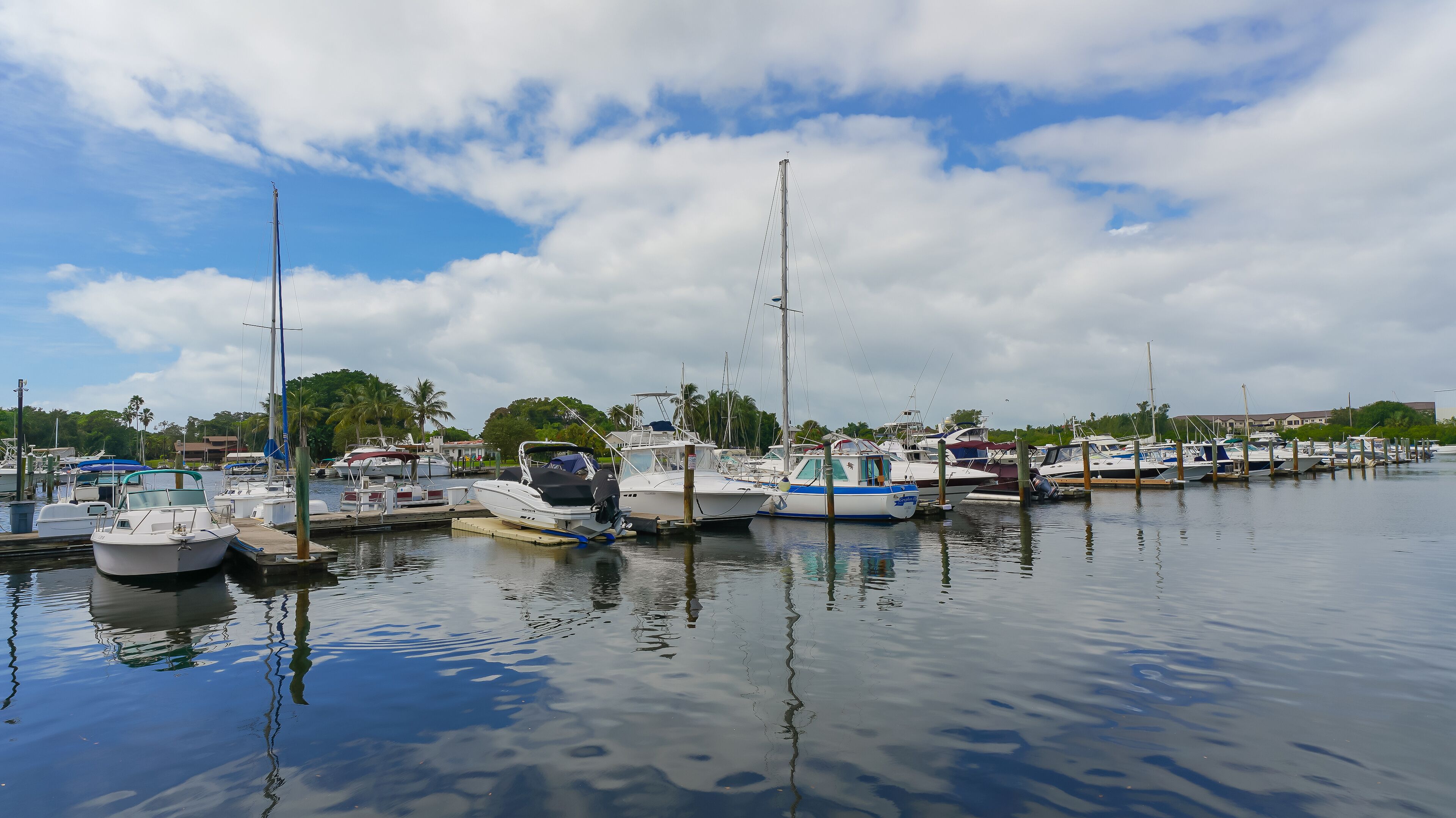 A marina with various boats docked, calm water, and a clear sky with clouds.