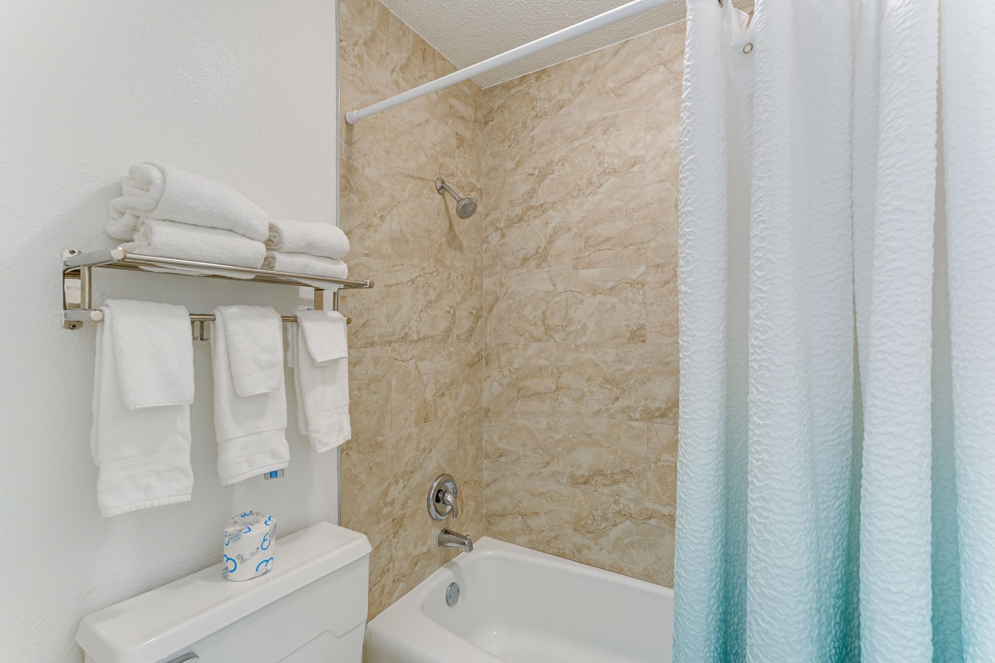 A bathroom with a bathtub, a towel rack with folded towels, and a toilet paper holder.