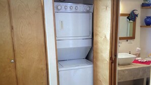 Un lavadero pequeño con lavadora y secadora integradas, un lavabo y un espejo sobre él.