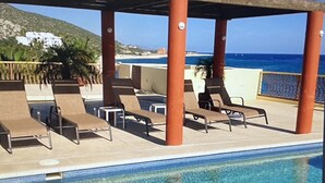 Zona junto a la piscina con sillones de descanso y vistas al océano.
