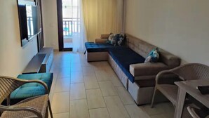 A living room with a sofa, a television, a chair, and a window with curtains. - luxury apartments in aldau heights with two pools 11514 (Hurghada)