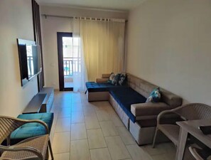 Ein Wohnzimmer mit einer Couch, einem Fernseher, einem Sessel und einem Fenster mit Vorhängen.