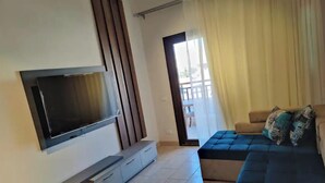 A modern living room with a flat-screen TV mounted on the wall, a sofa with patterned cushions, and a sliding glass door leading to an outdoor area. - luxury apartments in aldau heights with two pools 11514 (Hurghada)