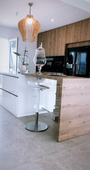 Een moderne keuken met een houten keukeneiland, witte barstoelen en een hanglamp.