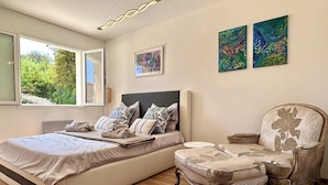 A bedroom with a large bed, a chair, and two paintings on the wall.