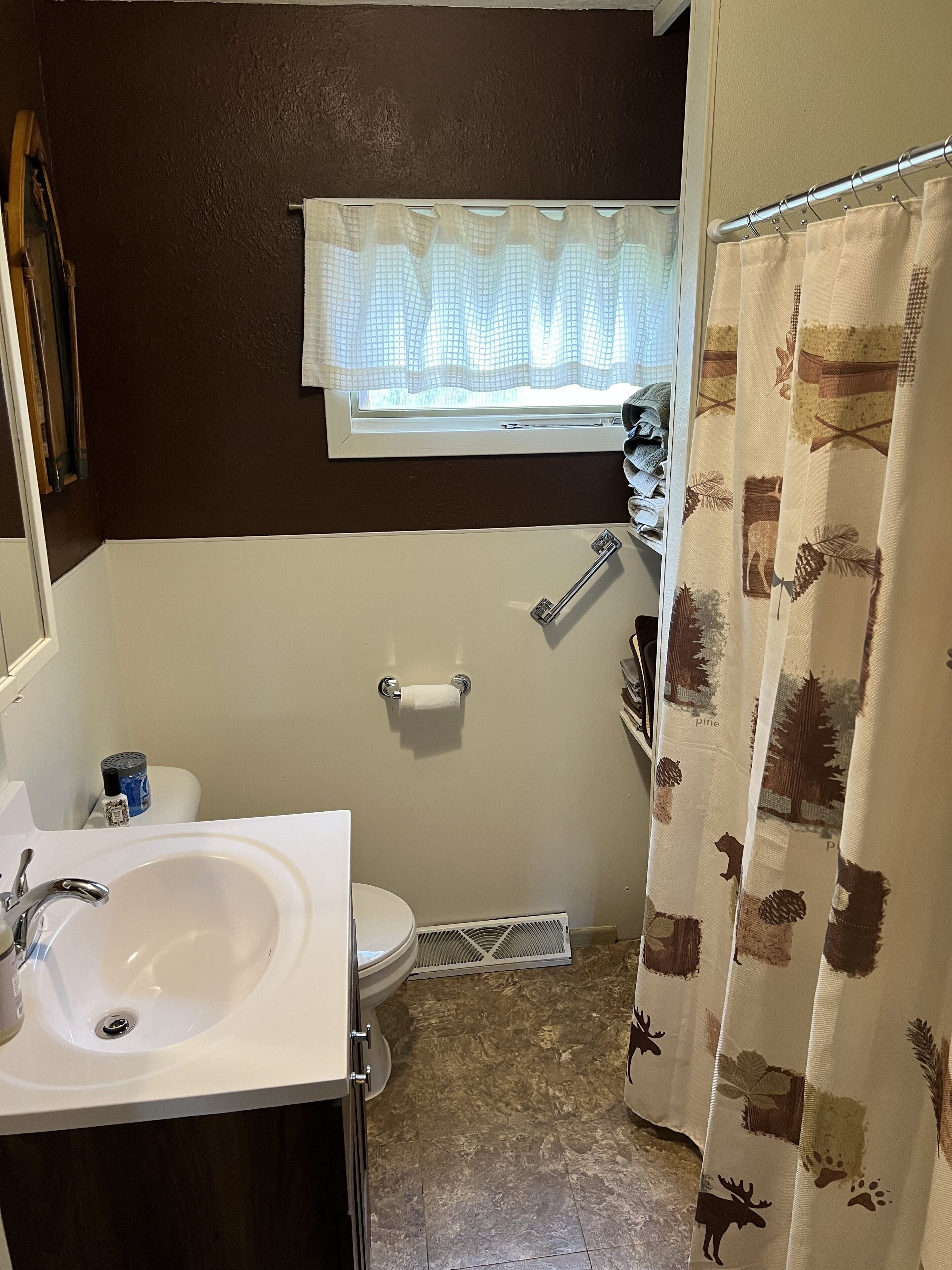 A bathroom with a white sink, a toilet, a window with a white curtain, and a shower curtain with animal prints.
